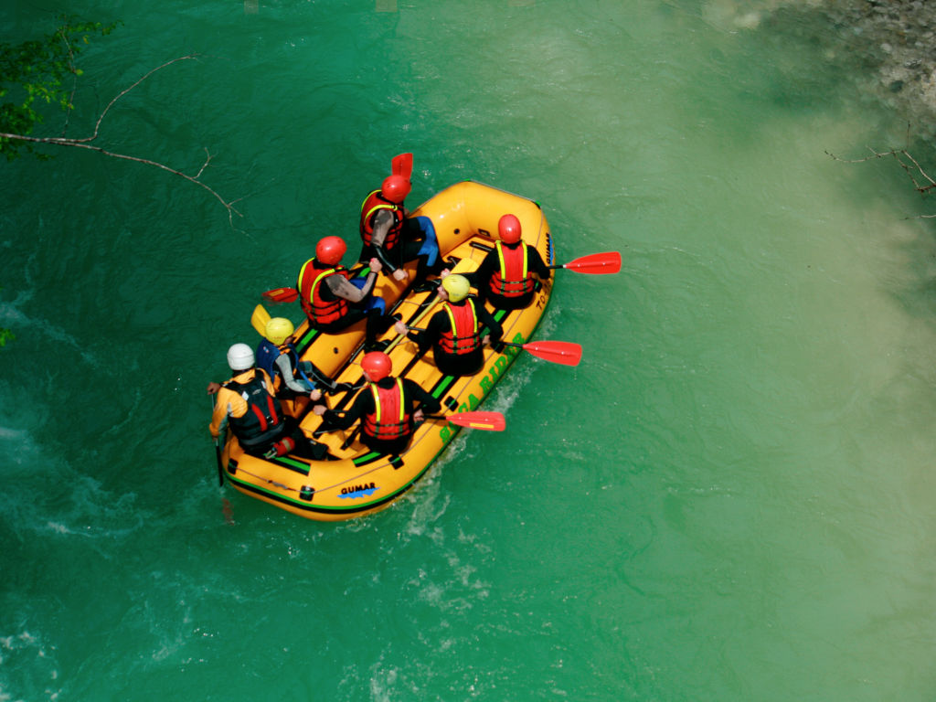 Rafting a Soča folyón. A raftosok a raft hajó szélén ülnek és eveznek a túravezető utasításai alapján.